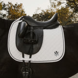 Black and white saddle on a horse with trees in the background. Sixteen Cypress