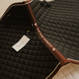 Quilted equestrian saddle pad with brand tag and logo on a dark background