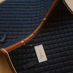 Navy quilted saddle pad with brown trim and Cypress Equestrian tag.