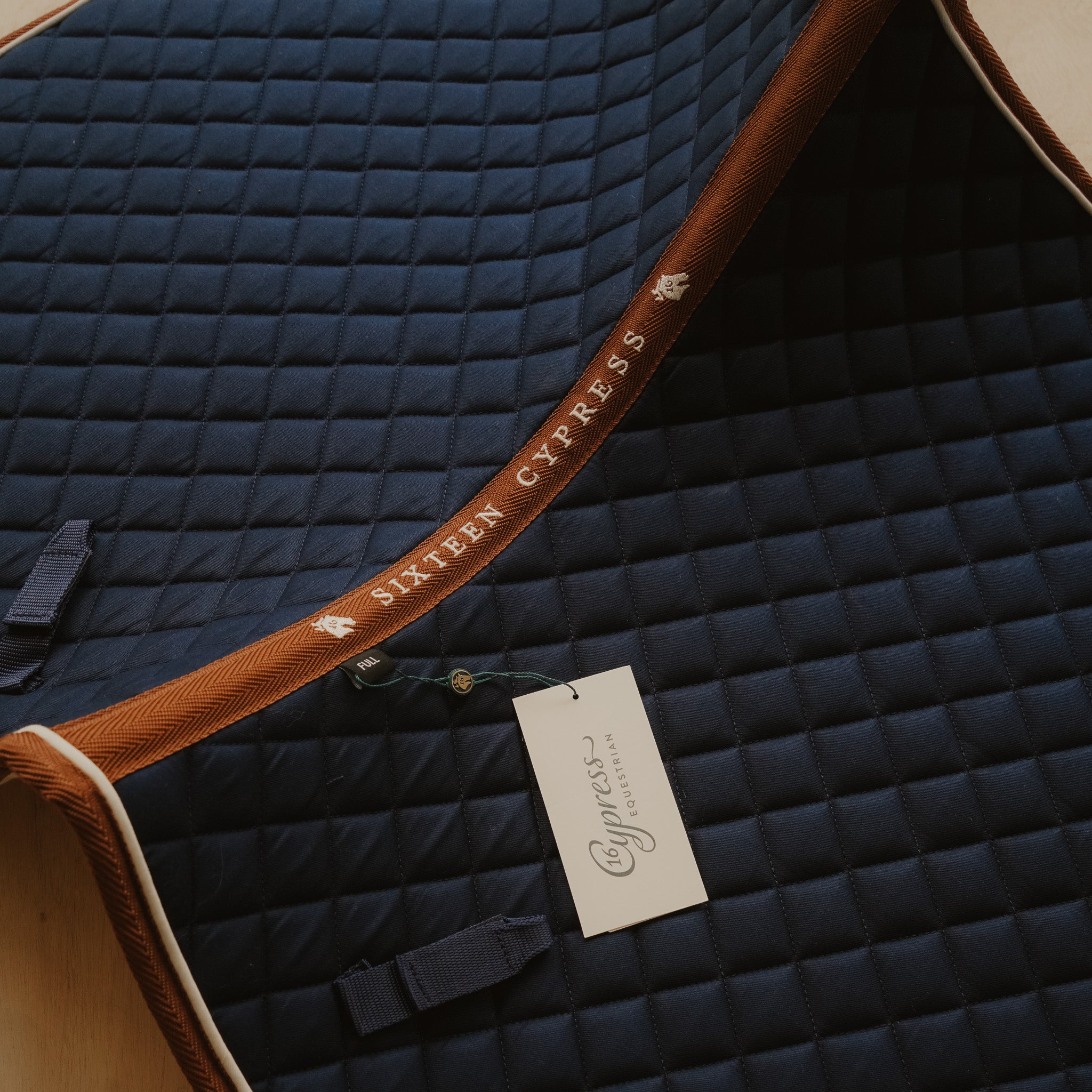 Navy quilted saddle pad with brown trim and Cypress Equestrian tag.