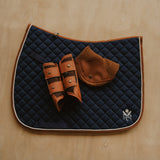 Navy quilted saddle pad with brown leather accessories on a wooden surface