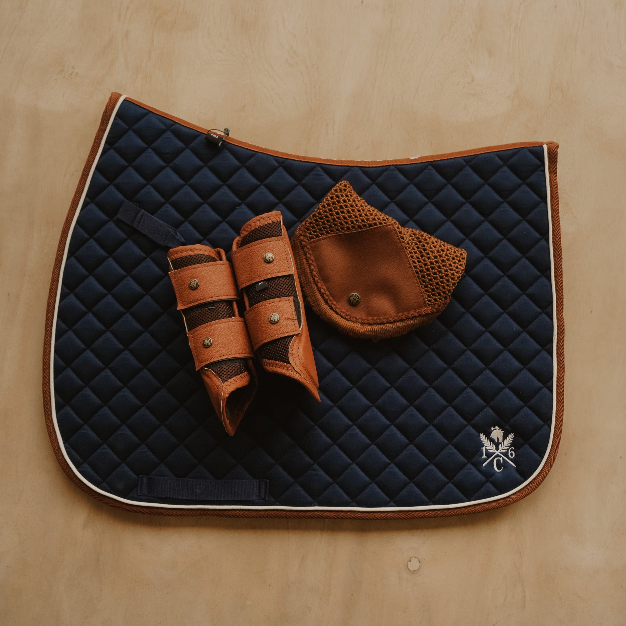 Navy quilted saddle pad with brown leather accessories on a wooden surface