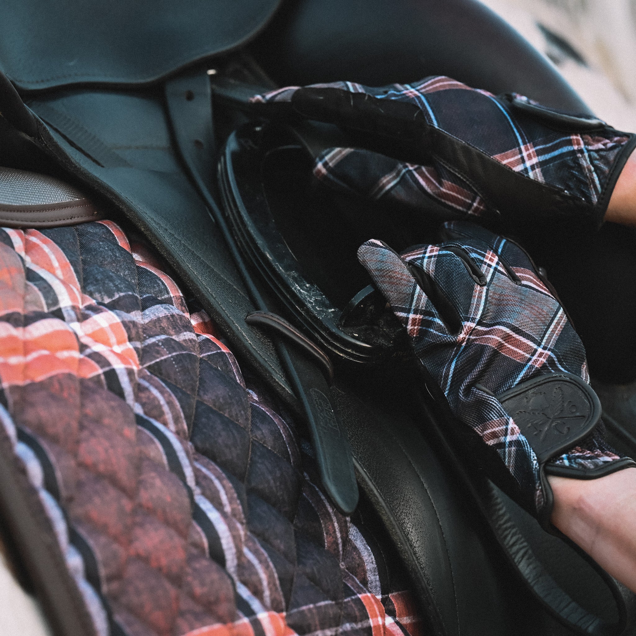 Person wearing sixteen cypress plaid gloves adjusting a saddle on a horse